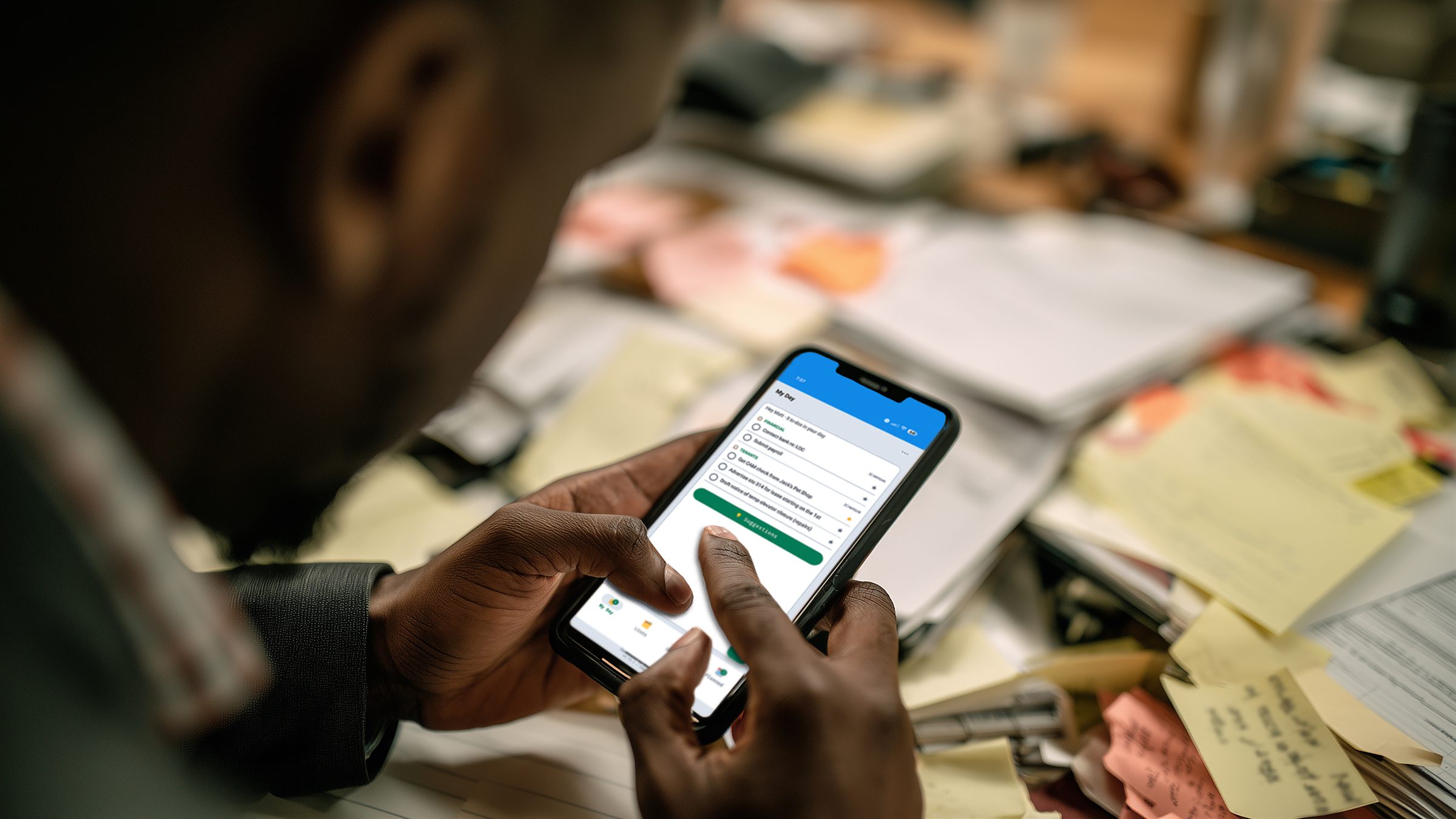 A person on their phone using the Checklists app's My Day view, over a desk covered in handwritten paper notes