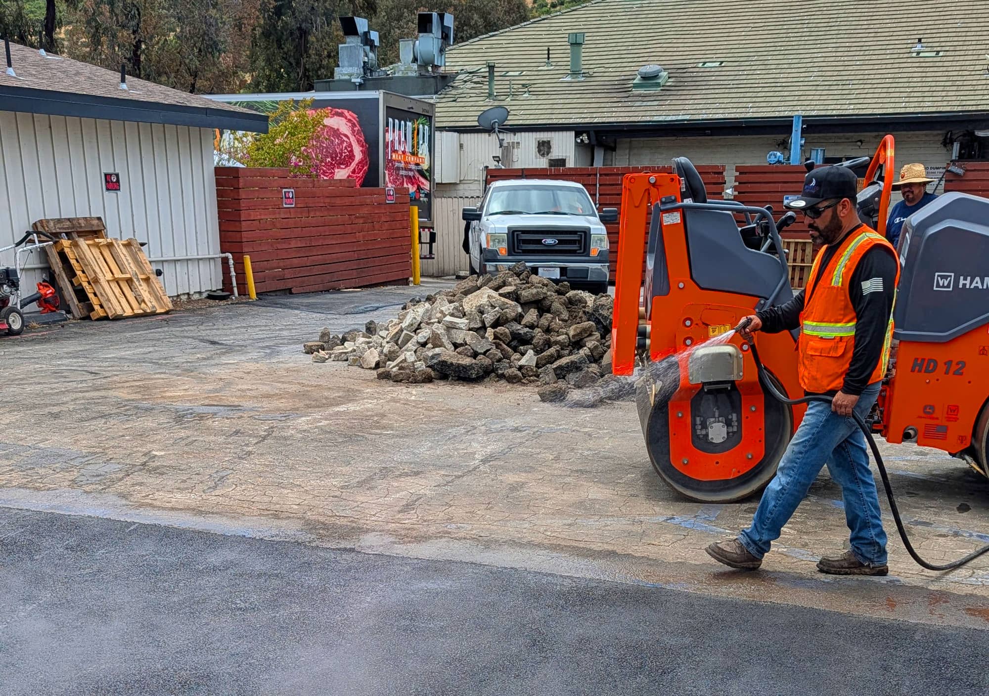 A contractor in a hi-vis vest doing paving work in a commercial property lot